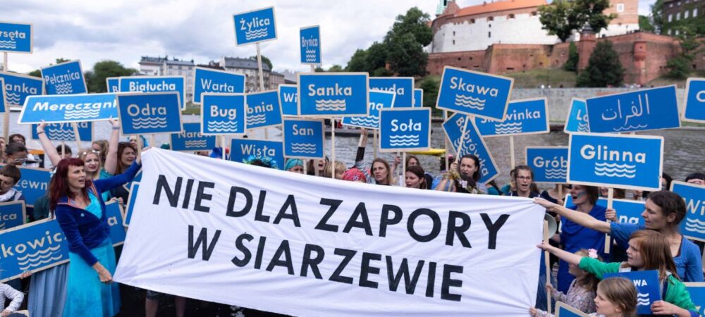 Protest przeciw budowie zapory w Siarzewie – uczestnicy stoją w wodzie z tablicami nazw polskich rzek